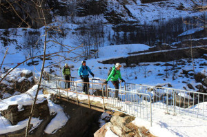 Sciatori su una pista da fondo attraversano un ponticello sulla Sesia. 